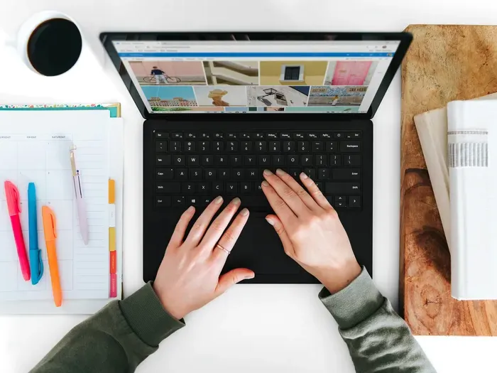 Overhead view of a person typing on a laptop with notebooks, pens, and coffee cup on a white desk on localservicelookup.com
